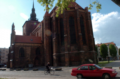 Na zdjęciu widzimy Kościół Maricacki, w tle drzewa, przed kościołem rowerzystę i zaparkowany czerwony samochód