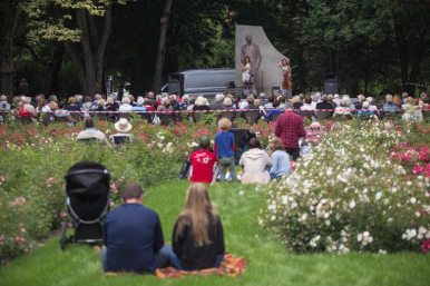 zielony park Waldorffa - uczestnicy koncertu siedzą  na trawie odwróceni na pierwszym planie dwie artystki, jedna z wiolonczela