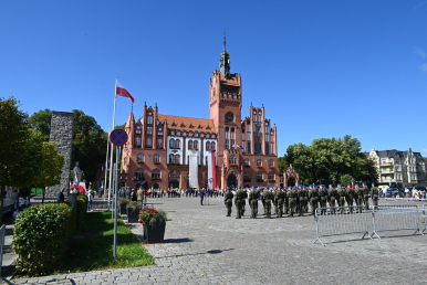 zdjęcie poglądowe, w tle ratusz, na pl. Zwycięstwa Wojsko RP, uczestnicy ur. z lat ubiegłych, pomnik Żołnierza Polskiego i miejska zieleń