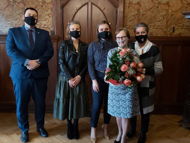 Na zdjęciu widzimy cztery kobiety i jednego mężczyznę; jedna z kobiet trzyma kwiaty, wszystkie osoby są w maseczkach, zdjęcie wykonano w zabytkowym gabinecie Prezydenta Miasta Słupska