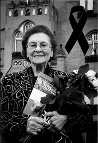 Na zdjęciu widzimy Panią Janinę trzymającą kwiaty, album o Słupsku a w tle ratusz słupski