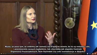 Na zdjęciu widzimy Martę Makuch Wiceprezydentkę Miasta Słupska, która mówi "Myślę, że poza tym,że widzimy jak zmienia się krajobraz miasta, bo są to remonty i ulic, i powstawanie nowych bydynków, tak  chociażby jak Słupskie Centrum Organizacji Pozarządowych, Dom Sąsiedzki czy cała rewitalizacja w Słupsku". W tle widzimy fragmenty flag Polski i Unii Europejskiej.