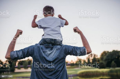 mężczyzna z dzieckem na ramionach unoszący ręce do góry