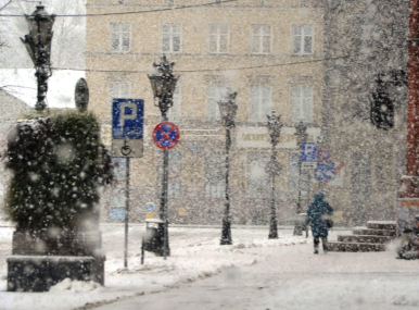 Widok na pl. Zwycięstwa i chodnik przy ratuszu, lampy, znaki drogowe, schody do ratusza i bardzo dużo śniegu i sypiący opad