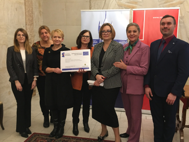 Na tle loga miasta Słupska i Uniwersytetu Pomorskiego widzimy Dyrektorkę Zespołu Szkół Ekonomicznych w Słupsku Panią Renatę Draszanowską trzymającą w dłoni plakat projektu obok niej jest dyrektowka Wydziału Edukacji,  Prezydentka miasta Słupska Krystyna Danilecka-Wojewódzka i Wiceprezydentka Beata Chrzanowska wraz z przedstawicielami Uniwersytetu Pomorskiego w Słupsku
