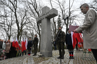 Krzyż katyński na cmentarzu, goście uroczystości, w tym przedstawiciele wojska, flagi Rzeczypospolitej Polskiej