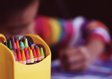 kolorowe kredki w pojemniku, w tle rysujące dziecko; Zdjęcie wykonane przez Free-Photos dla Pixabay