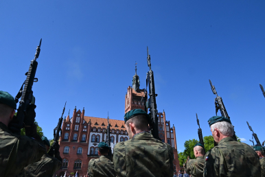 Żołnierze trzymający broń, w tle ratusz miejski