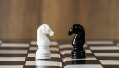 Dwie figury szachowe - skoczek biały i skoczek czarny na szachownicy.