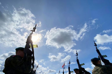 Na zdjęciu widzimy żołnierzy z podniesionymi do góry karabinami oraz słoneczne niebo z białymi chmurami