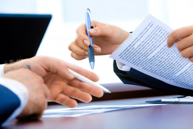 Grafika przedstawia dłonie dwóch osób z długopisami, dokumentem oraz laptopem w tle. Fot. Pixabay.