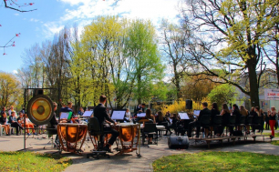 zielony park Waldorffa uczestnicy koncertu siedzą  na  krzesełkach, na pierwszym planie orkiestra z rozstawionymi pulpitami i instrumentami