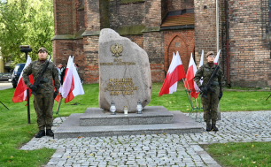 Dwaj Żołnierze Wojska Polskiego trzymają wartę podczas uroczystości; na środku Pomnik Polskiego Państwa Podziemnego ; w tle  Kościół Mariacki