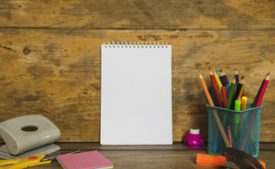 Zdjęcie przedstwia biurko z artykułami szkolnymi: dziurkacz, nożyczki, zszywacz, kredki w pojemniku i notatnik.