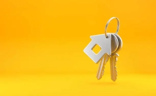 Zdjęcie przedstawia pęk kluczy z brylokiem w kształcie domu na żółtym tle