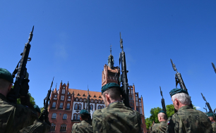 Żołnierze trzymający broń, w tle ratusz miejski