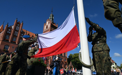 Żołnierze wieszający flagę państwową na maszt- w tle ratusz słupski