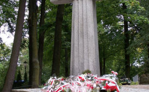 Na zdjęciu widzimy betonowy krzyż z napisem KATYŃ, przed którym znajdują się wiązanki kwiatów
