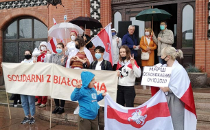 Na zdjęciu widzimy grupę ludzi z transparentem z napisem SOLIDARNI Z BIAŁORUSIĄ. Osoby znajdujące się na zdjęciu układają palce u dłoni w znaj V - na znak solidarności i zwycięstwa.