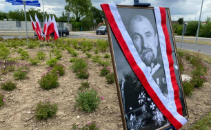 Na zdjęciu widzimy flagi Rzeczypospolitej Polskiej, tabliczki z nazwą ronda - RONDO GEN. TADEUSZA ROZWADOWSKIEGO oraz zdjęcie patrona przesłonięte szarfą w kolorach białym i czerwonym