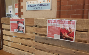 zdjęcie dwóch drewnianych skrzynek, na ich przodzie przyczepione kartki informujące o akcji "Zostań Świętym Mikołajem"