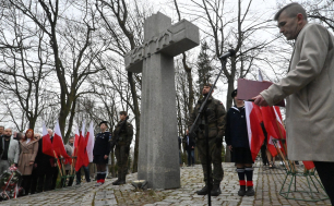 Na zdjęciu widać Krzyż Katyński i żołnierzy stojących obok; w tle uczestnicy ubiegłorocznych uroczystości i flagi RP