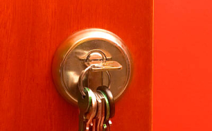 Na zdjęciu widzimy czerwone drzwi z pękiem kluczy w zamku.