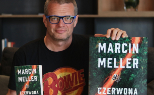 Dziennikarz Marcin Meller w pozycji siedzącej na kolanach opiera dwie książki "Czerwona Ziemia"