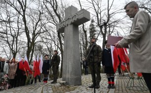 Krzyż Katyński, w tle goście uroczystości upamiętniających ofiary, przedstawiciele wojska, flagi RP