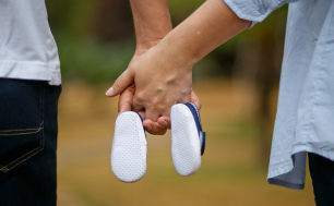 Grafika przedstawia parę stojącą tyłem trzymającą w złączonych dłoniach dziecięce buciki. (fot.pixabay).