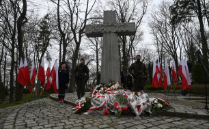 Zdjęcie poglądowe z ub. lat z uroczystości upamiętniającej datę 17 września; Krzyż Katyński,wiązanki kwiatów, żołnierze oraz flagi państwowe, w tle drzewa