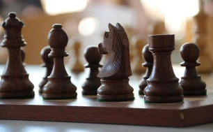 Ciemne figury szachowe na szachownicy: wieża, konik, laufer, królówka.