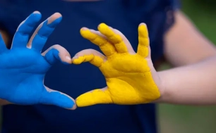 Na zdjęciu widzimy pomalowane dłonie dziecka. Jedna dłoń jest pomalowana na niebiesko druga na żółto.