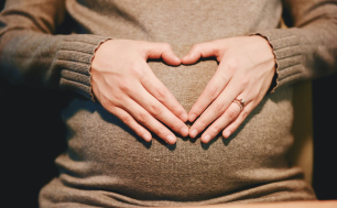 na zdjęciu widzimy  dłonie złożone w kształt serca na brzuchu ciężarnej kobiety.