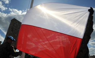 Flaga Rzeczypospolitej Polskiej trzymana przez żołnierzy na tle niebieskiego nieba