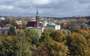 Na zdjęciu widzimy kościół św. Jacka, ceglaną budowlę ze strzelistą wieżą, oprócz tego dużo zieleni, drzew i panoramę miasta Słupska