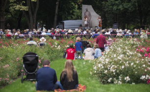 zielony park Waldorffa uczestnicy koncertu siedzą  na trawie odwróceni na pierwszym planie dwie artystki, jedna z wiolonczela