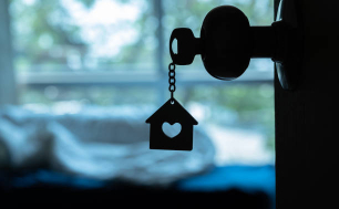 Na zdjęciu widzimy klucz do domu z brelokem domowym w dziurce od klucza na drewnianych drzwiach