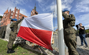 Żołnierza zapinający flagę RP na masz, w tle ratusz