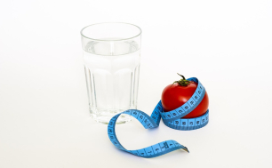 Na zdjęciu szklanka z wodą, pomidor owinięty centymetrem