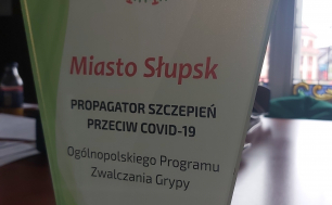 Na zdjęciu widzimy statuetkę z napisem MIASTO SŁUPSK PROPAGATOR SZCZEPIEŃ PRZECIWKO COVID-19, OGÓLNOPOLSKI PROGRAM ZWALCZANIA GRYPY,23 WRZEŚNIA 2021 R