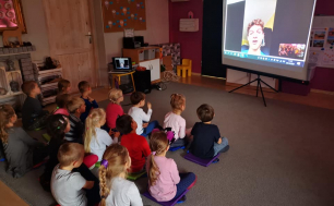 dzieci siedzące na dywanie słuchające bajkę czytaną przez mężczyznę - spotkanie on-line,  czytający widoczny na ekranie, połączenie przez intermnet