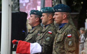 Troje żołnierzy trzymających złożoną flagę RP na rękach