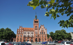 ratusz, przed ratuszem zaparkowane na parkingu samochody, błękitne niebo