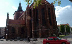 Na zdjęciu widzimy Kościół Maricacki, w tle drzewa, przed kościołem rowerzystę i zaparkowany czerwony samochód