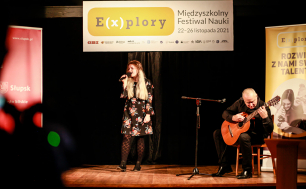 Zdjęcie przedstawia występ woklany uczennicy  oraz grającego na gitarze nauczyciela z Zespołu Szkół Ekonomicznych w Słupsku, w tle baner z napisem: E(x)plory Miedzyszkolny Fetiwal Nauki