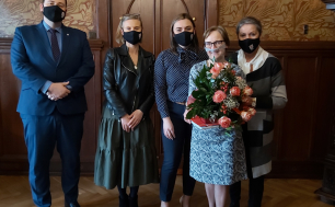 Na zdjęciu widzimy cztery kobiety i jednego mężczyznę; jedna z kobiet trzyma kwiaty, wszystkie osoby są w maseczkach, zdjęcie wykonano w zabytkowym gabinecie Prezydenta Miasta Słupska