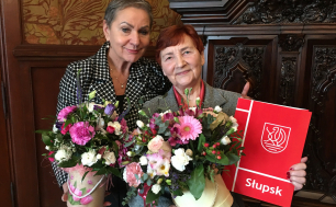 Prezydentka Słupska z Krystyną Homentą -obie Pani trzymają kwiaty, Pani Homenda dodatkowo teczkę z listem.