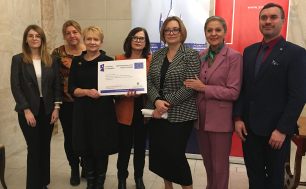 Na tle loga miasta Słupska i Uniwersytetu Pomorskiego widzimy Dyrektorkę Zespołu Szkół Ekonomicznych w Słupsku Panią Renatę Draszanowską trzymającą w dłoni plakat projektu obok niej jest dyrektowka Wydziału Edukacji,  Prezydentka miasta Słupska Krystyna Danilecka-Wojewódzka i Wiceprezydentka Beata Chrzanowska wraz z przedstawicielami Uniwersytetu Pomorskiego w Słupsku